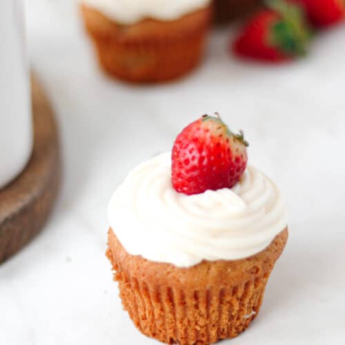 Prosecco Cupcake on a white surface with strawberries in the background