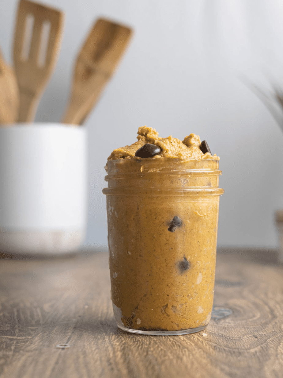 pumpkin cookie dough in a mason jar on a wood surface with utensil holder in background