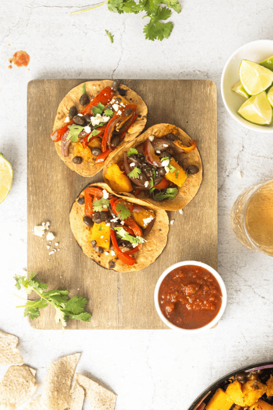 butternut squash tacos on a wooden cutting board with salsa next to them and cilantro