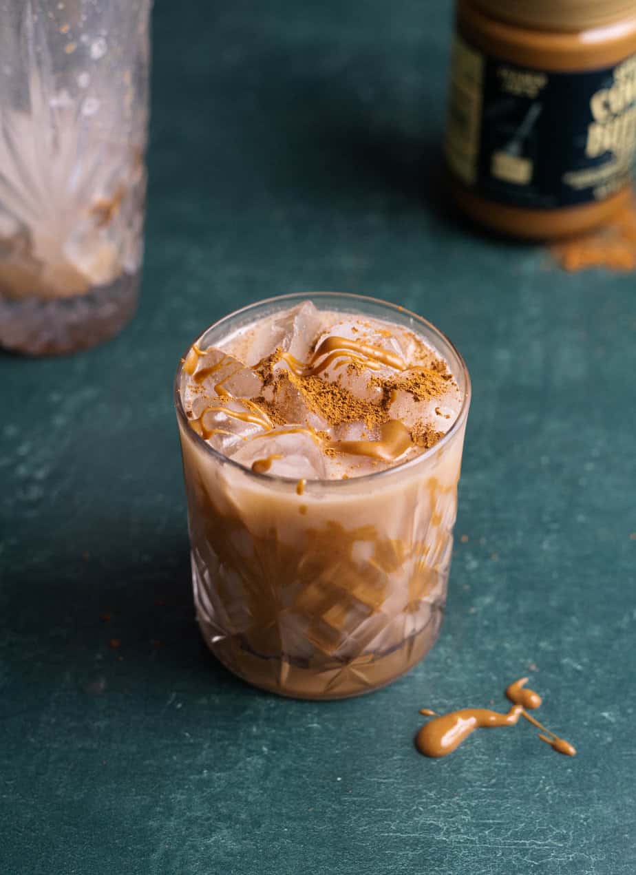 Creamy biscoff cocktail in a glass with biscoff dripped on top of it and cookies in the background 