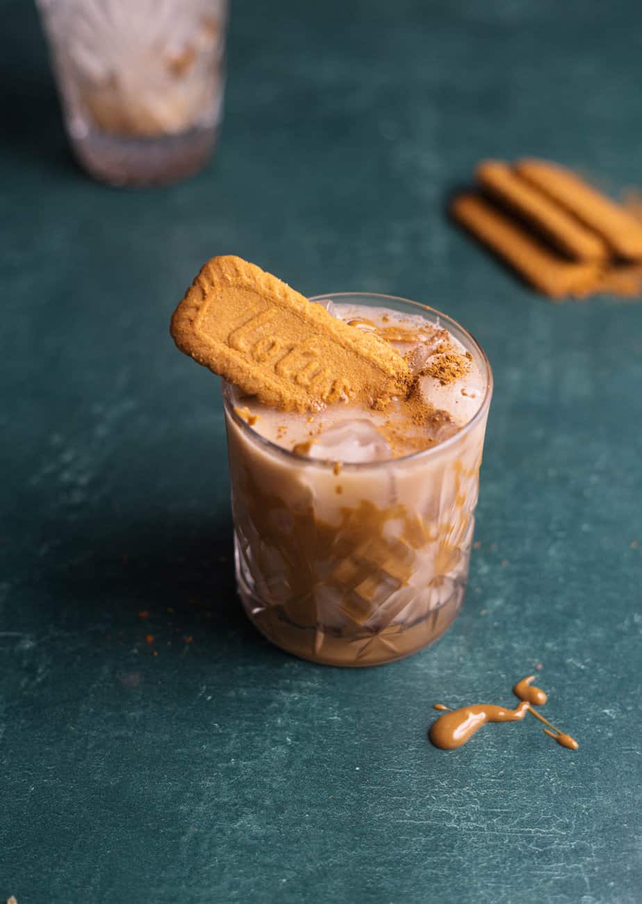 Lotus biscoff cocktail in a glass with a lotus biscoff cookie sticking out of the top  and the glass on a green surface