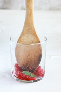 a wooden spoon muddling rapsberries and mint in a glass