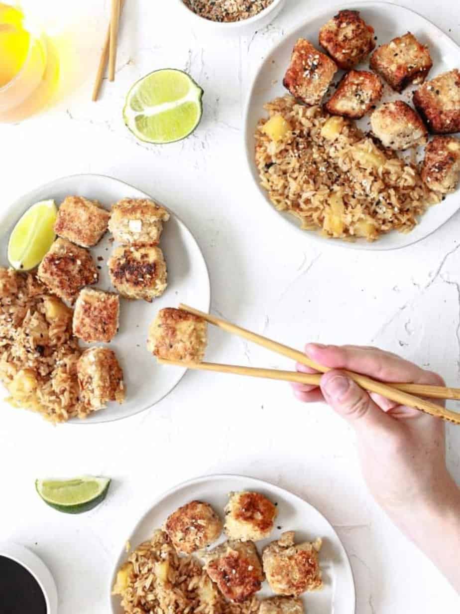 crispy coconut tofu on three plates with limes next to it and a chopstick holding on of the tofu pieces