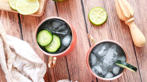 Flat lay of moscow mule with two mule glasses full of the cocktail and cucumber slices showing. Also there is a juicer and napking