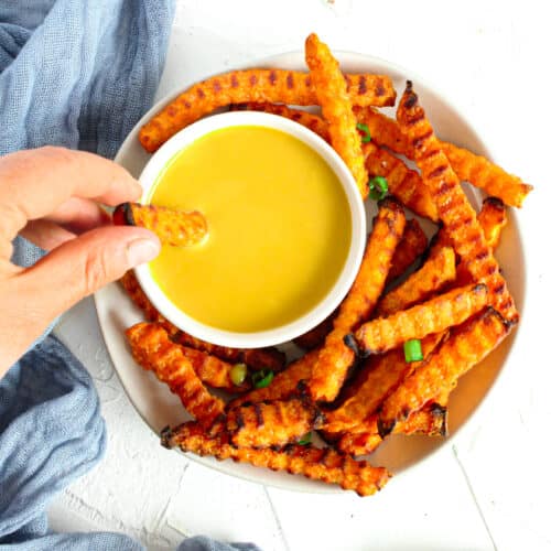 Air Fryer Sweet potato fries on a plate with honey mustard dipping sauce and the fry is being dunked into the sauce
