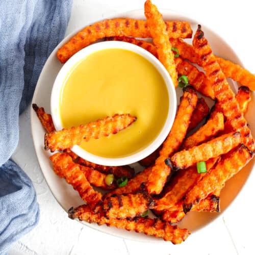 Honey Mustard Vegan Sauce in a small white bowl with sweet potato fries surronding it