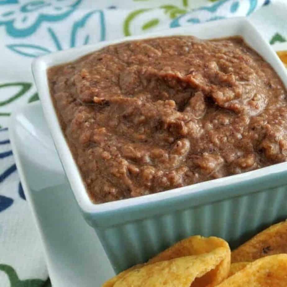 Black bean dip in a white bowl with chips next to it on a colorful flower surface