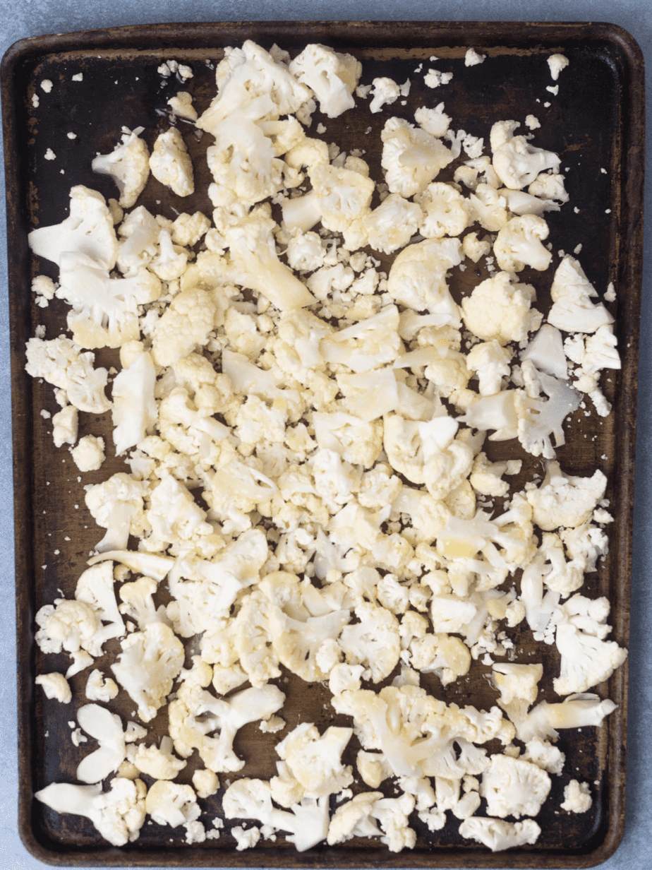 Raw cauliflower on a black baking sheet cut into bite size pieces before baking