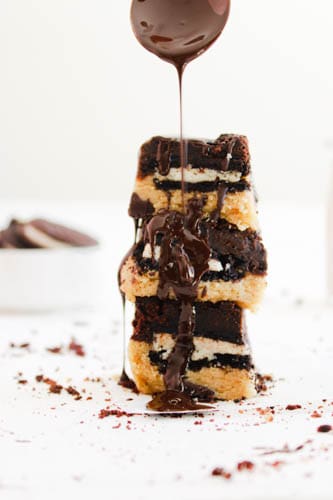 Vegan Slutty Brownies in a stack (3) with a white background and melted chocolate being dripped onto them