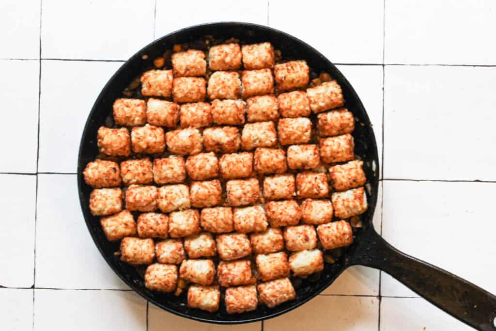 tater tots layered on top of veggies for vegan tater tot casserole in a skillet