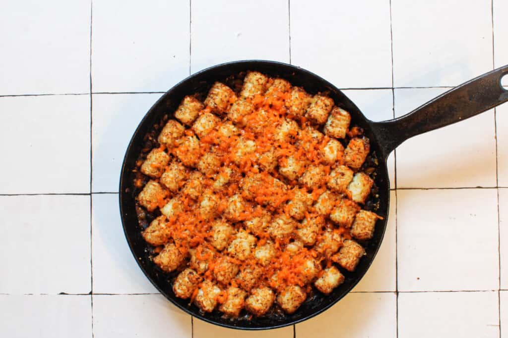 melted vegan cheese on top of tater tots in a cast iron skillet