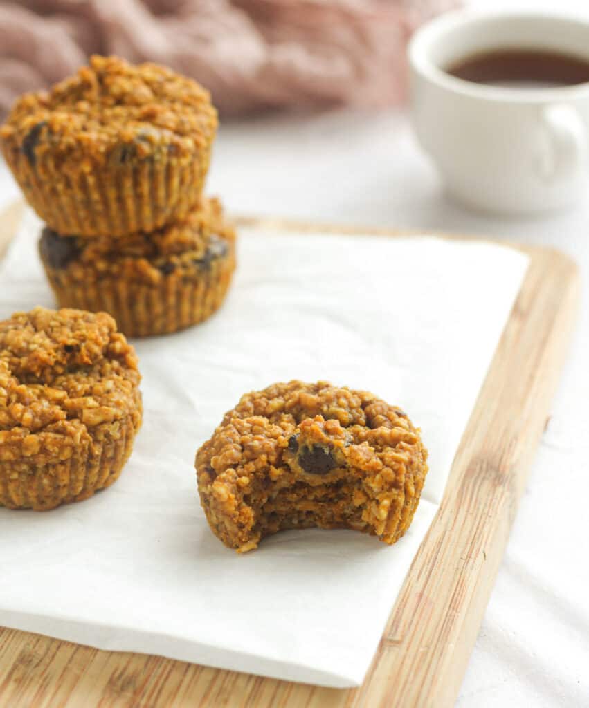 pumpkin protein muffin with a bite taken out on a cutting board, a cup of coffee in the background