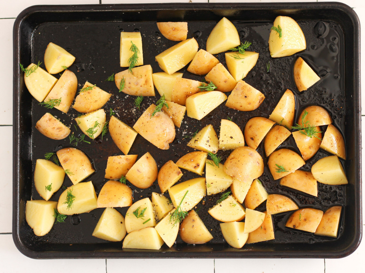 Cut potatoes with dill, olive oil, salt and pepper on top of them on a baking sheet before being cooked