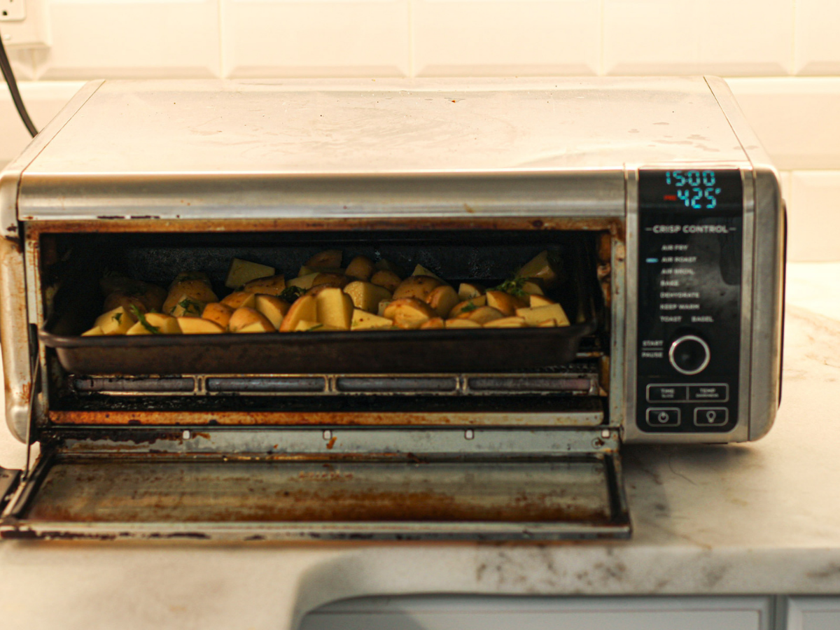 Tray of uncooked potatoes being placed into ninja foodi on countertop