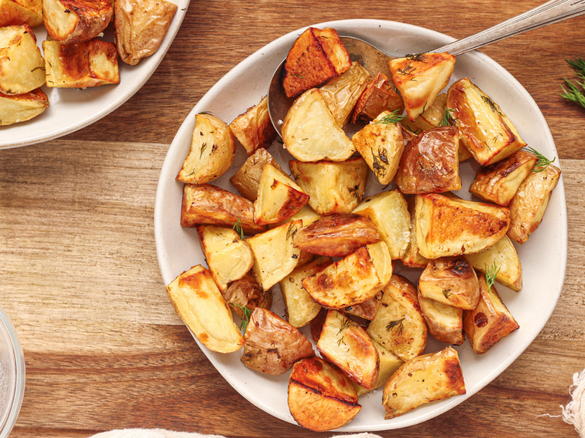 Ninja Foodi Roasted potatoes with dill on top on a white plate on a wood surface with lemon and dill next to the plate.