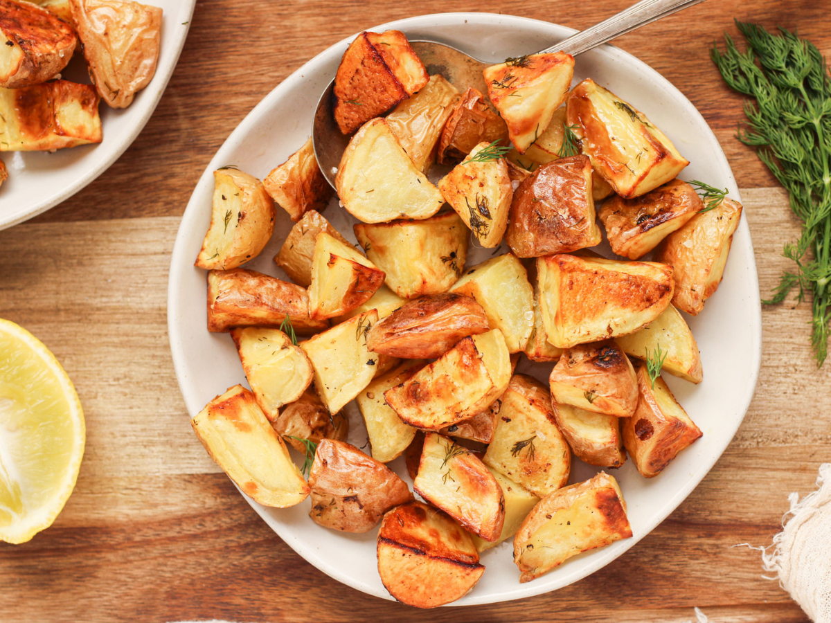 Ninja Foodi Roasted potatoes with dill on top on a white plate on a wood surface with lemon and dill next to the plate.