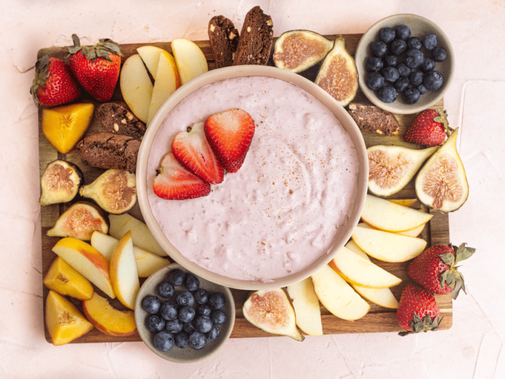 vegan fruit dip in a pink bowl with strawberries on top and fruit next to it