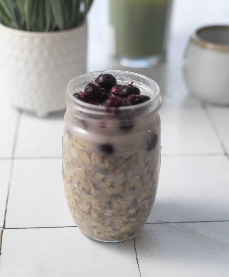 Oats in a mason jar with frozen fruit on top prior to be refrigerated 