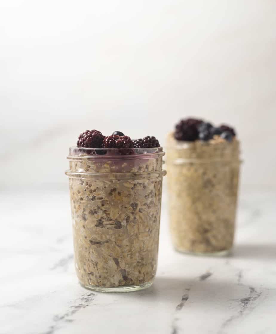 Overnight oats with frozen blackberries on top in a mason jar on a marble surface