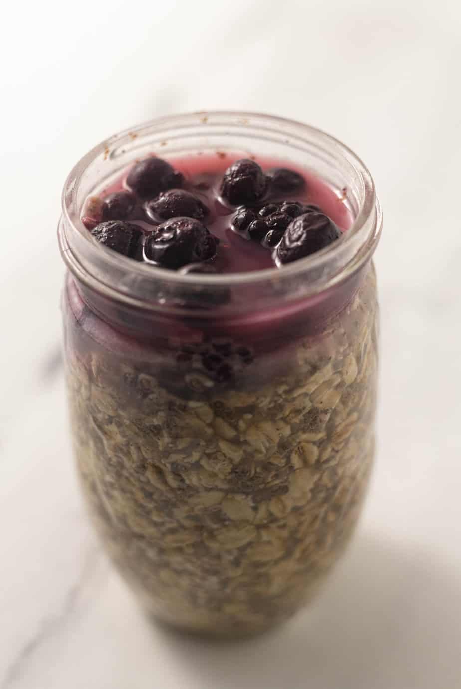 Oats in a mason jar with frozen fruit on top after being in the refrigerated  
