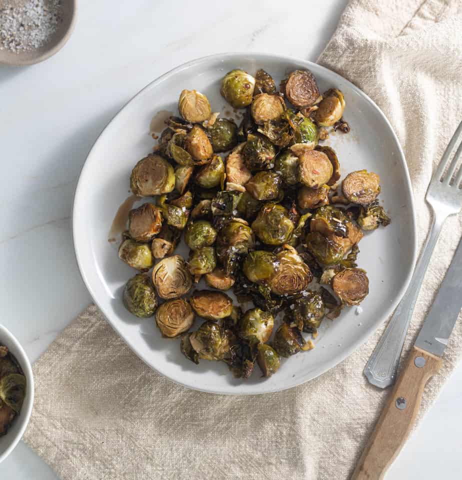 Balsamic Brussel Sprouts on a plate with a fork and knife next to it and a linen napkin