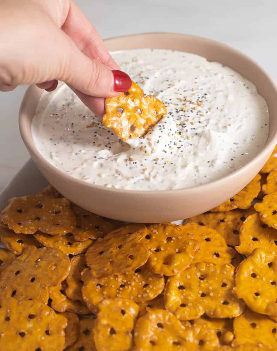 Everything but the bagel dip in a pink bowl with a pretzel thin dipping into the dip