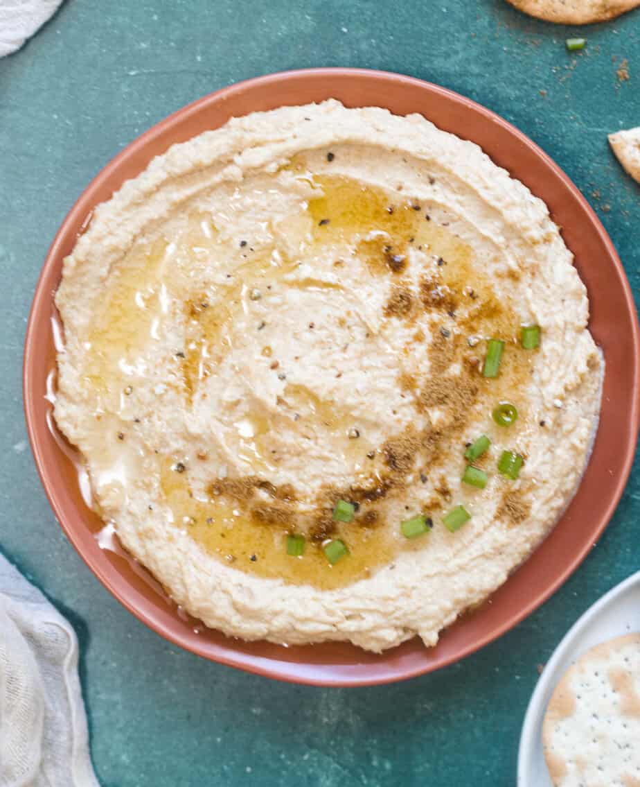 Hummus on an orange plate with olive oil, salt, pepper and chives on top