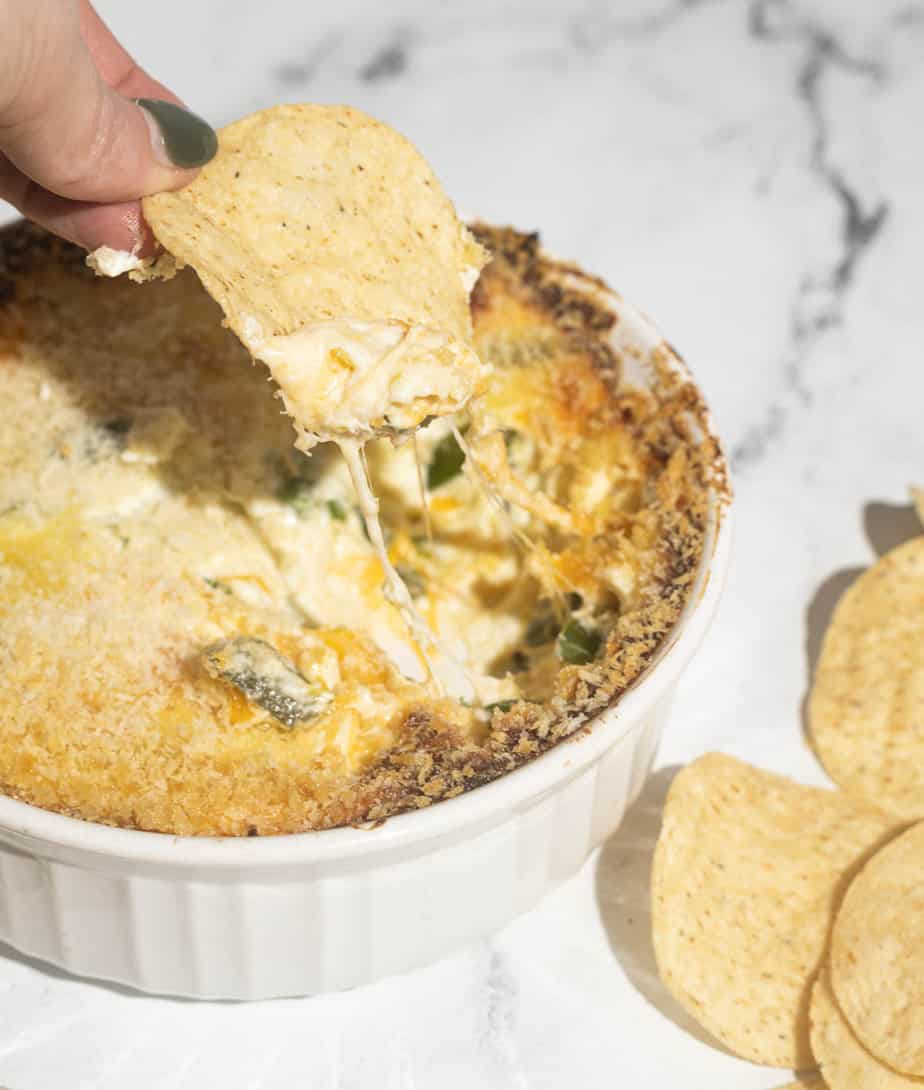 Jalapeno popper dip in a bowl with one chip dipping into the bowl and showing a cheese bowl