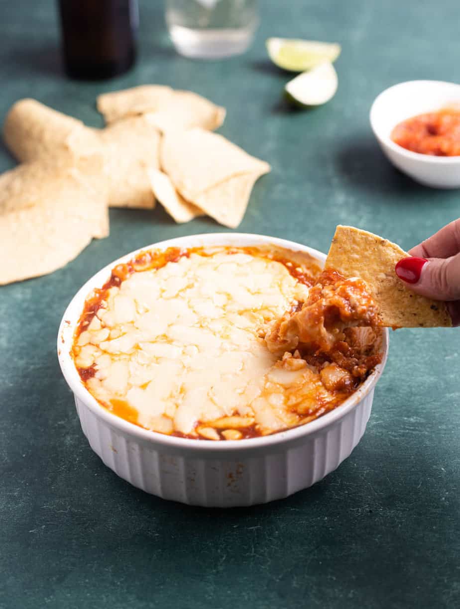 vegan bean dip in a white bowl with a chip being dipped into it