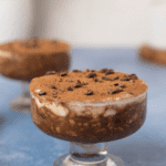 Tiramisu overnight oats in a glass jar with cocoa nibs and cocoa powder on top on a blue backdrop