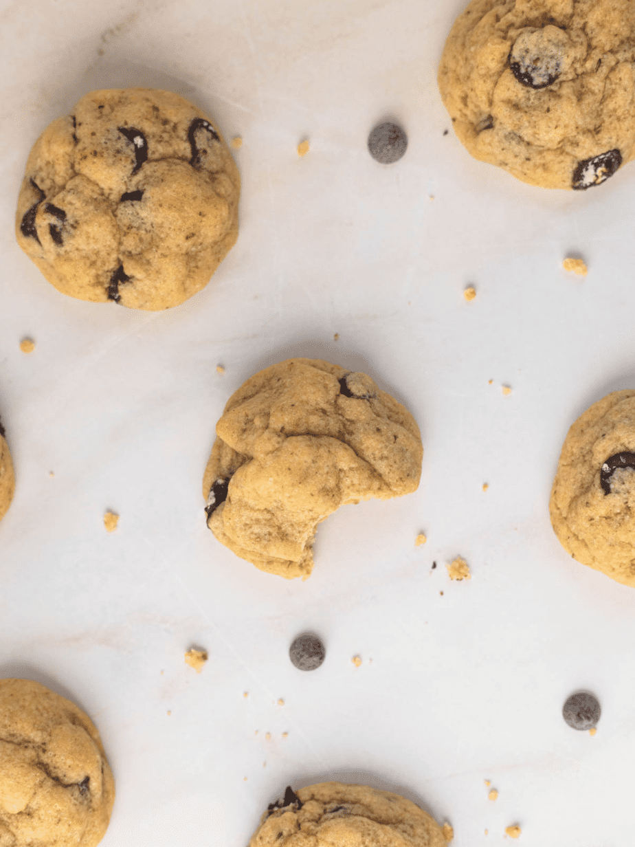 Chocolate chip cookies on a white background with bites taken out of the cookies and chocolate chips surrounding them