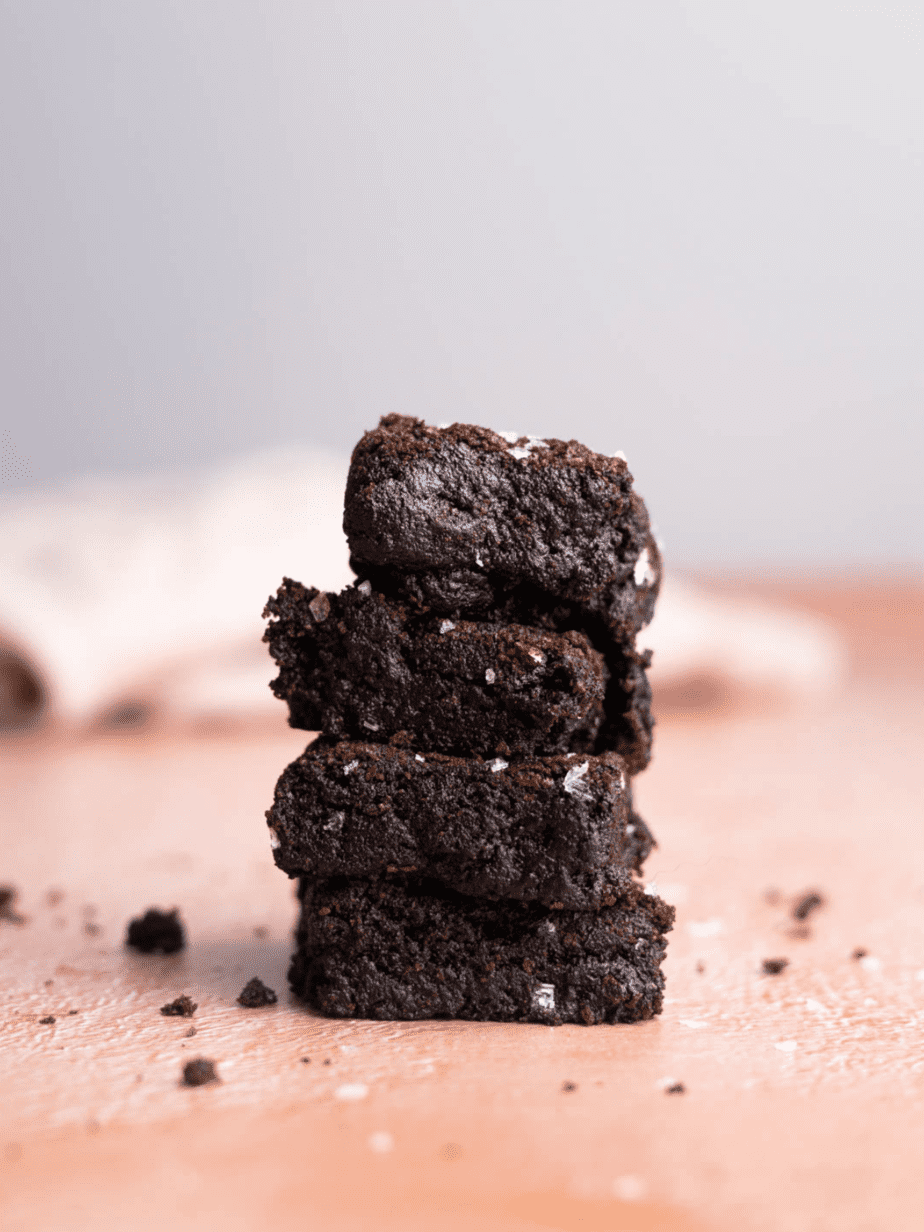 Dairy free brownies stacked on top of each other (four total) with flakey sea salt and a pink backdrop