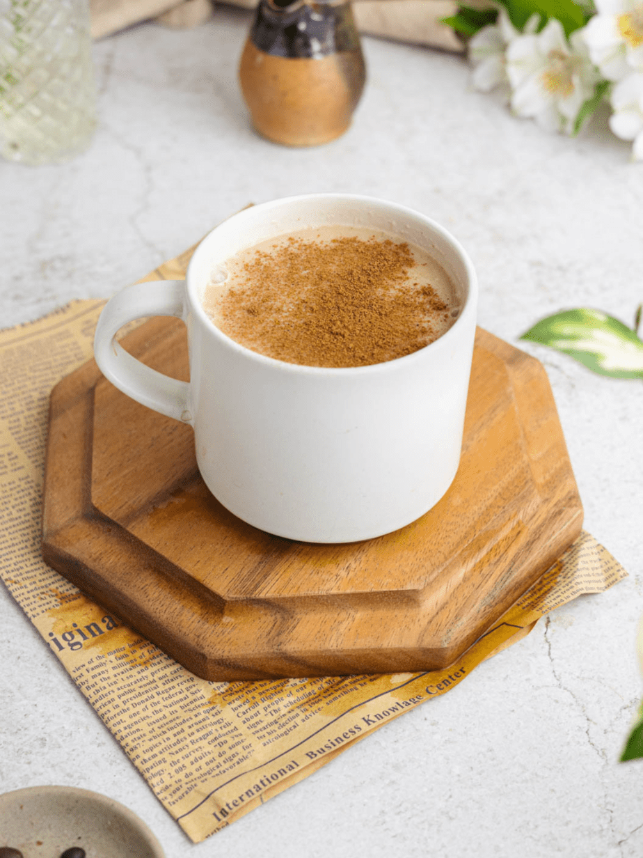 Maple latte in a mug with cinnamon on top on top of wood blocks