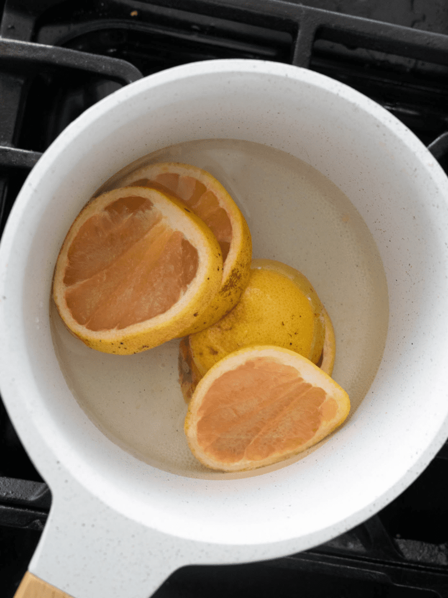 The grapefruit simple syrup being made with grapefruits, water and sugar in a white sauce pan