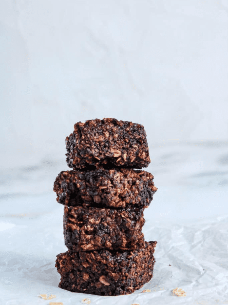 Protein brownies in a stack on parchment paper with oats by the bottom of them