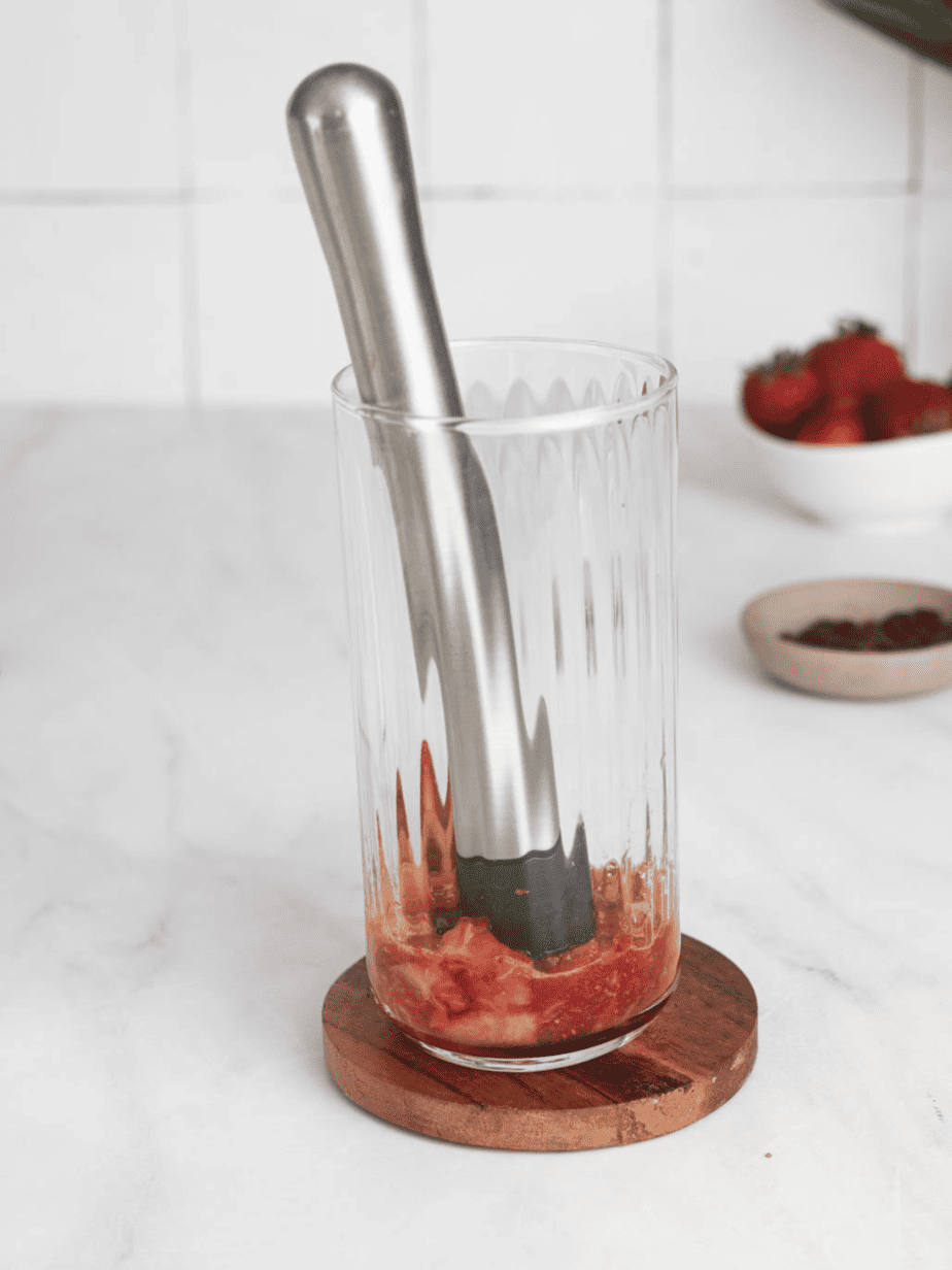 muddled strawberries in a glass with a muddler in the glass