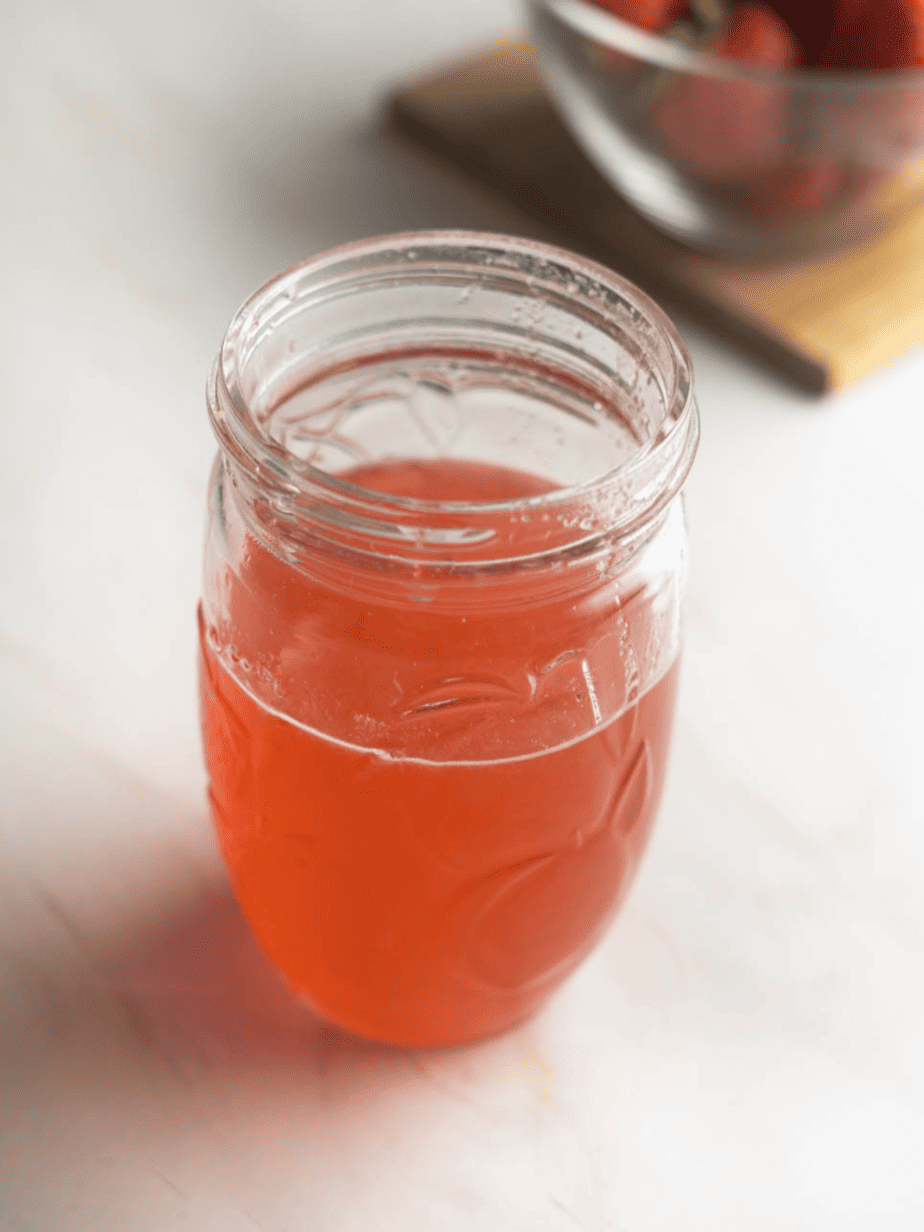 Strawberry simple syrup in a mason jar without lid strawberry bowl in background