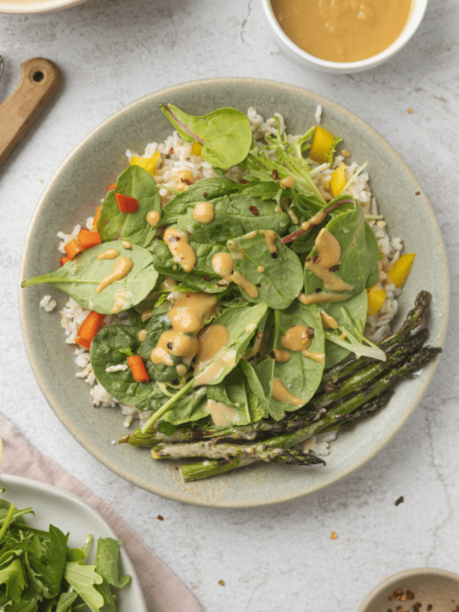 miso tahini dressing on a salad with apargus spinach and rice on a white table