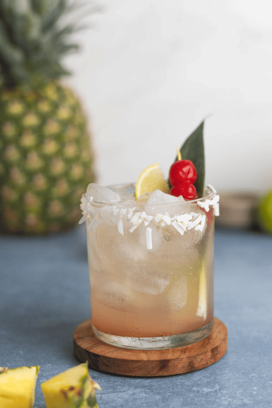 pina colada sangria in a glass with cherries lime and a pineapple leaf on a blue backdrop