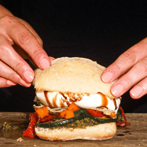 vegetarian burrata sandwich with two hands hold it showing the inside of the burrata sandwich while sitting on counting board