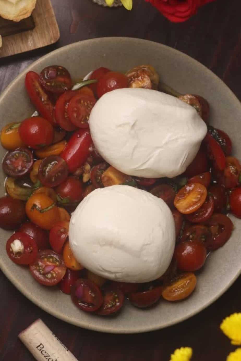 burrata caprese salad with the burrata on top of the dressed tomatoes on a green plate