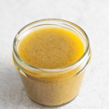 maple dijon vinaigrette in a small mason jar on a white surface showing the inside of the sauce on an angle
